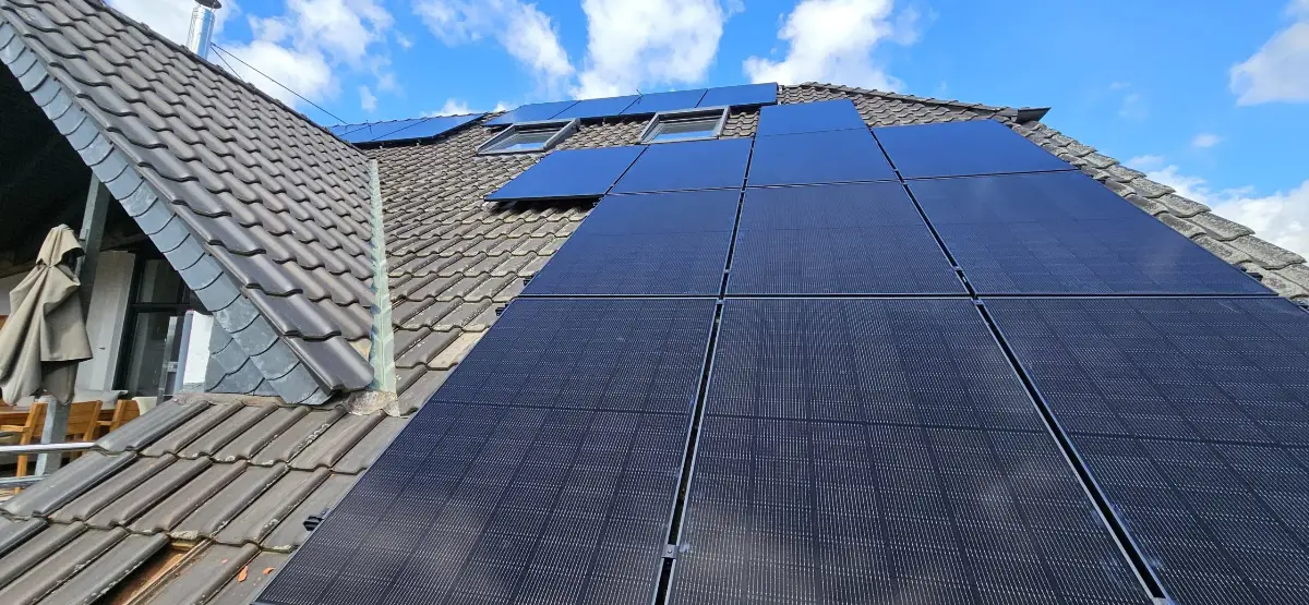 Dunkle Photovoltaikmodule auf einem Steildach, daneben zwei Dachfenster