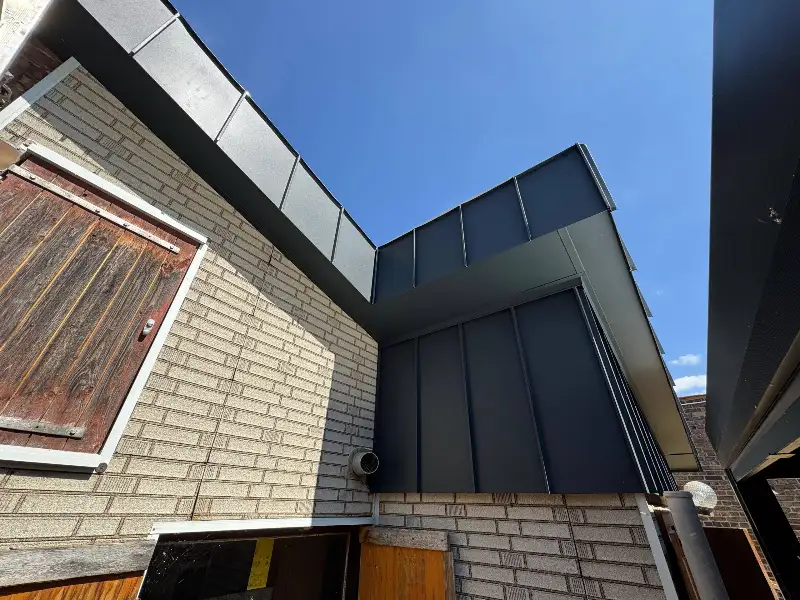 Anbau mit dunkler Metallverkleidung an einer hellen Klinkerwand, von unten gegen den Himmel fotografiert